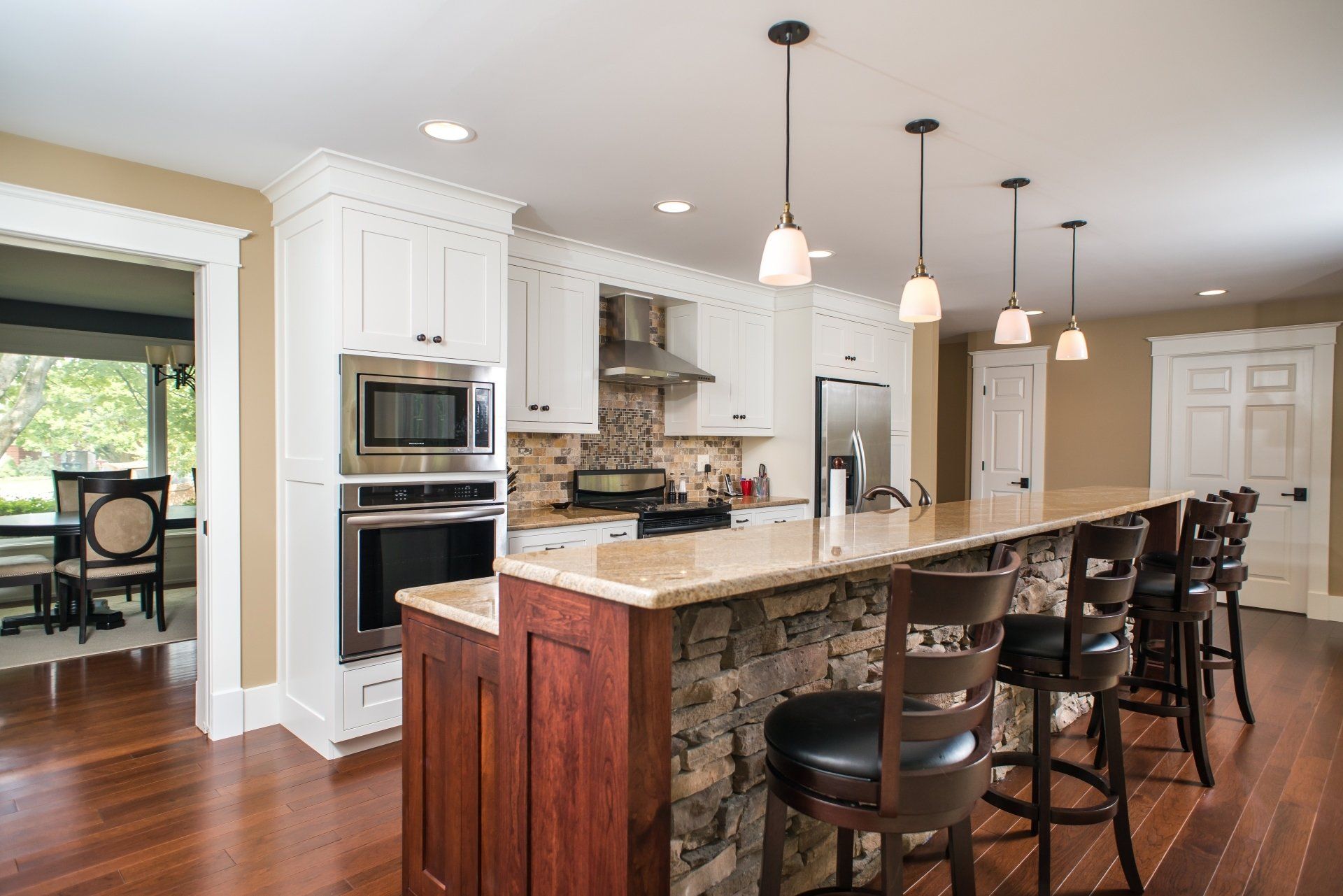 Bright kitchen with white cabinets, granite island, pendant lights, and hardwood floors