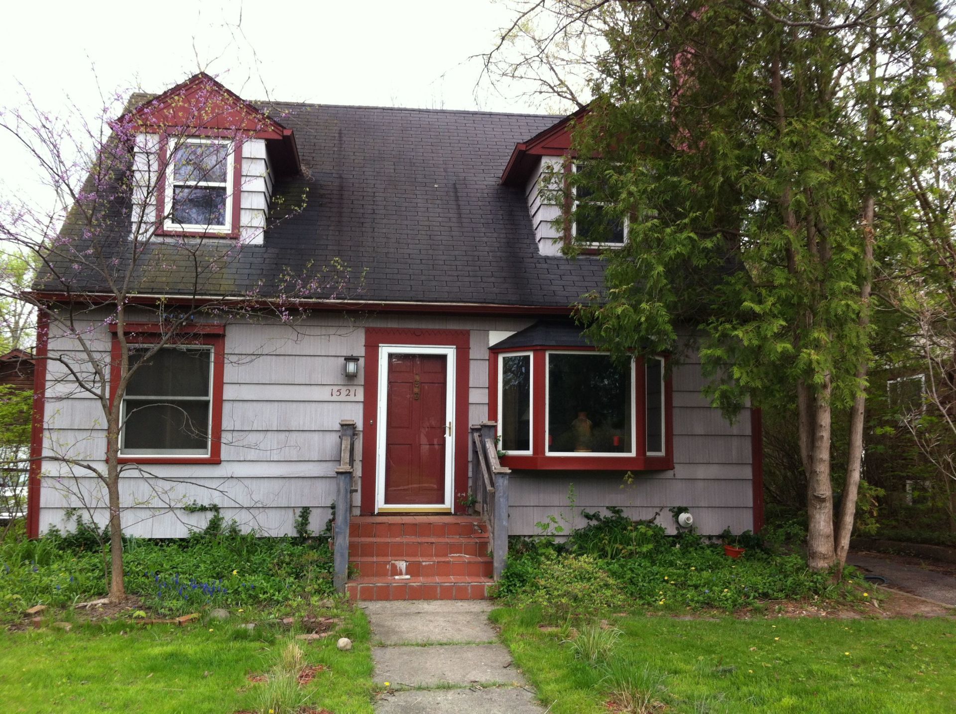 Small gray house with red trim, front steps, and trees in the yard