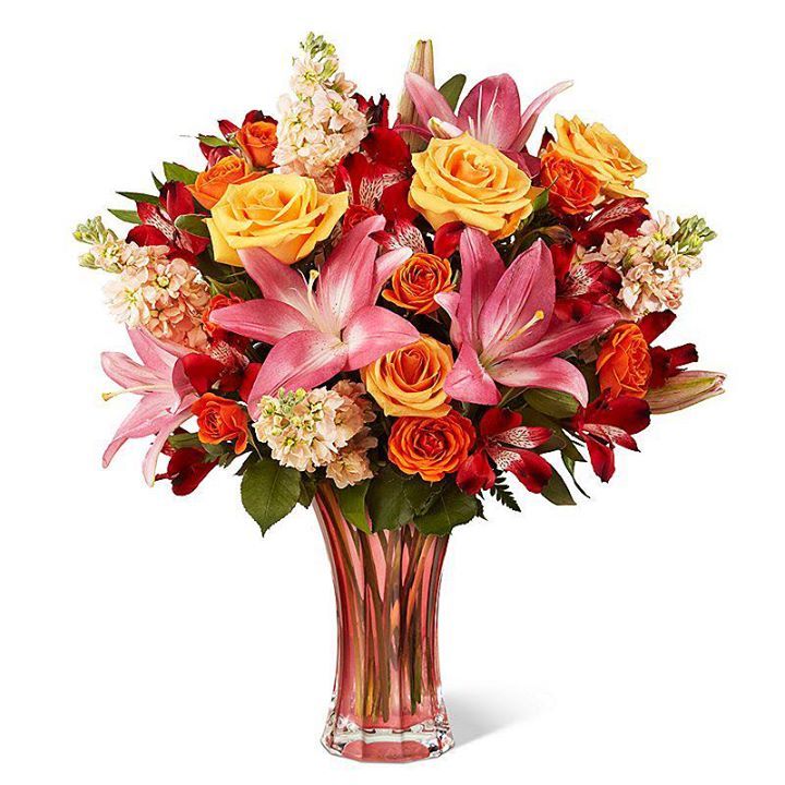 Bouquet of pink lilies, yellow roses, and red flowers in a clear glass vase