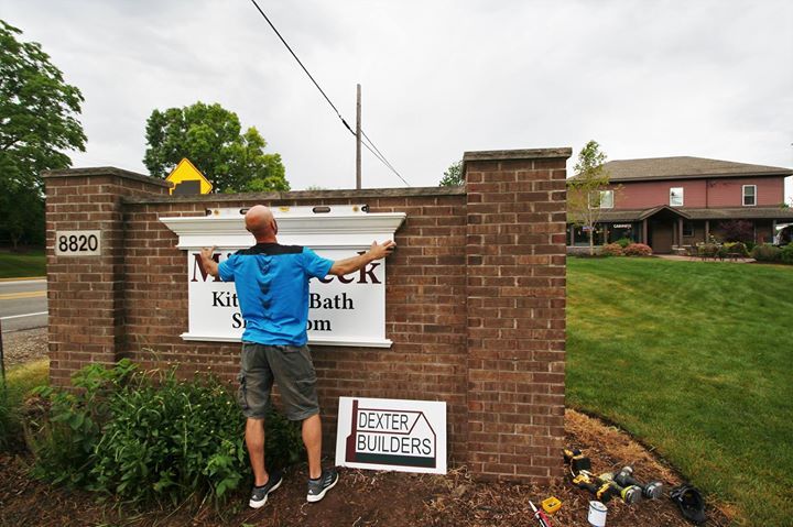 Worker installing sign on brick entrance pillar outside a residential community.