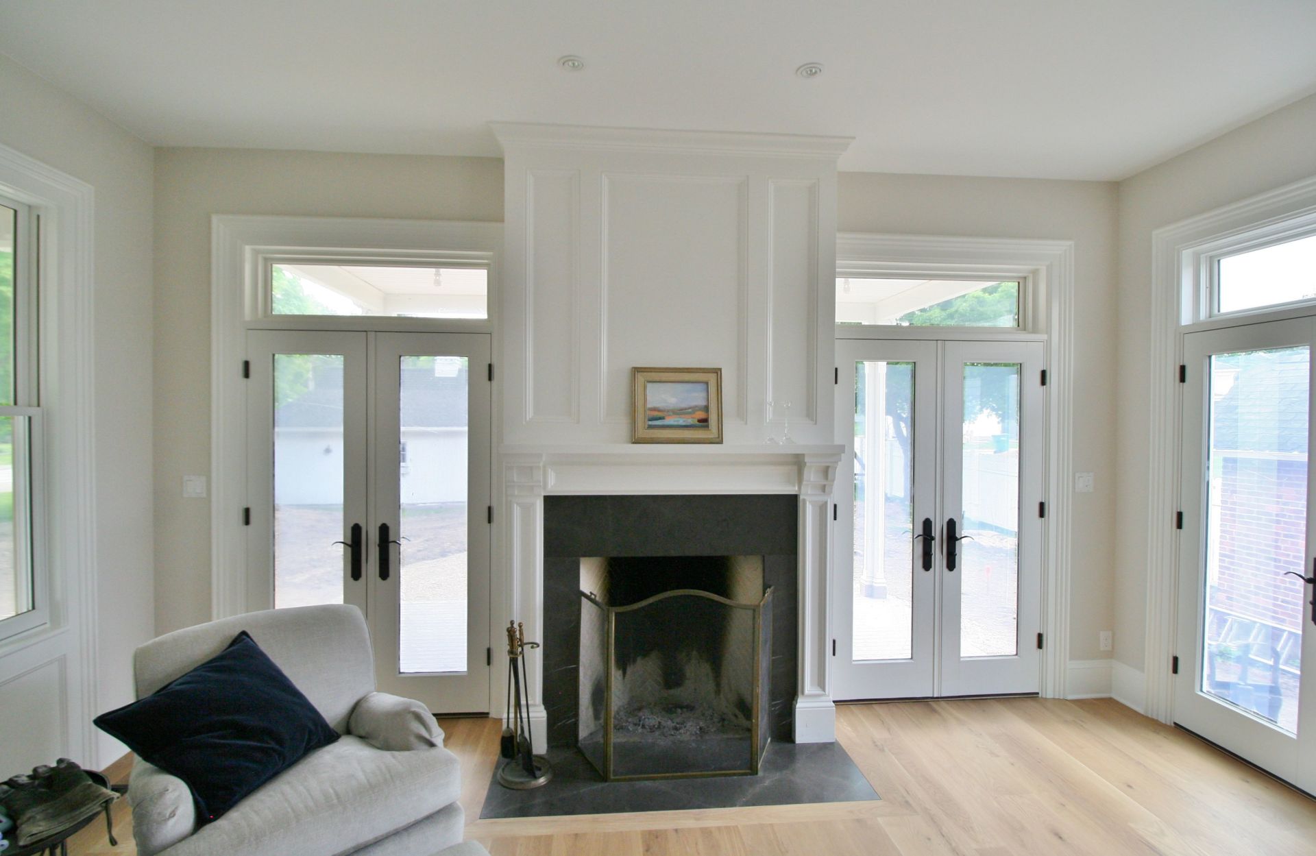 Bright living room with fireplace, white walls, hardwood floors, and tall windows and doors.