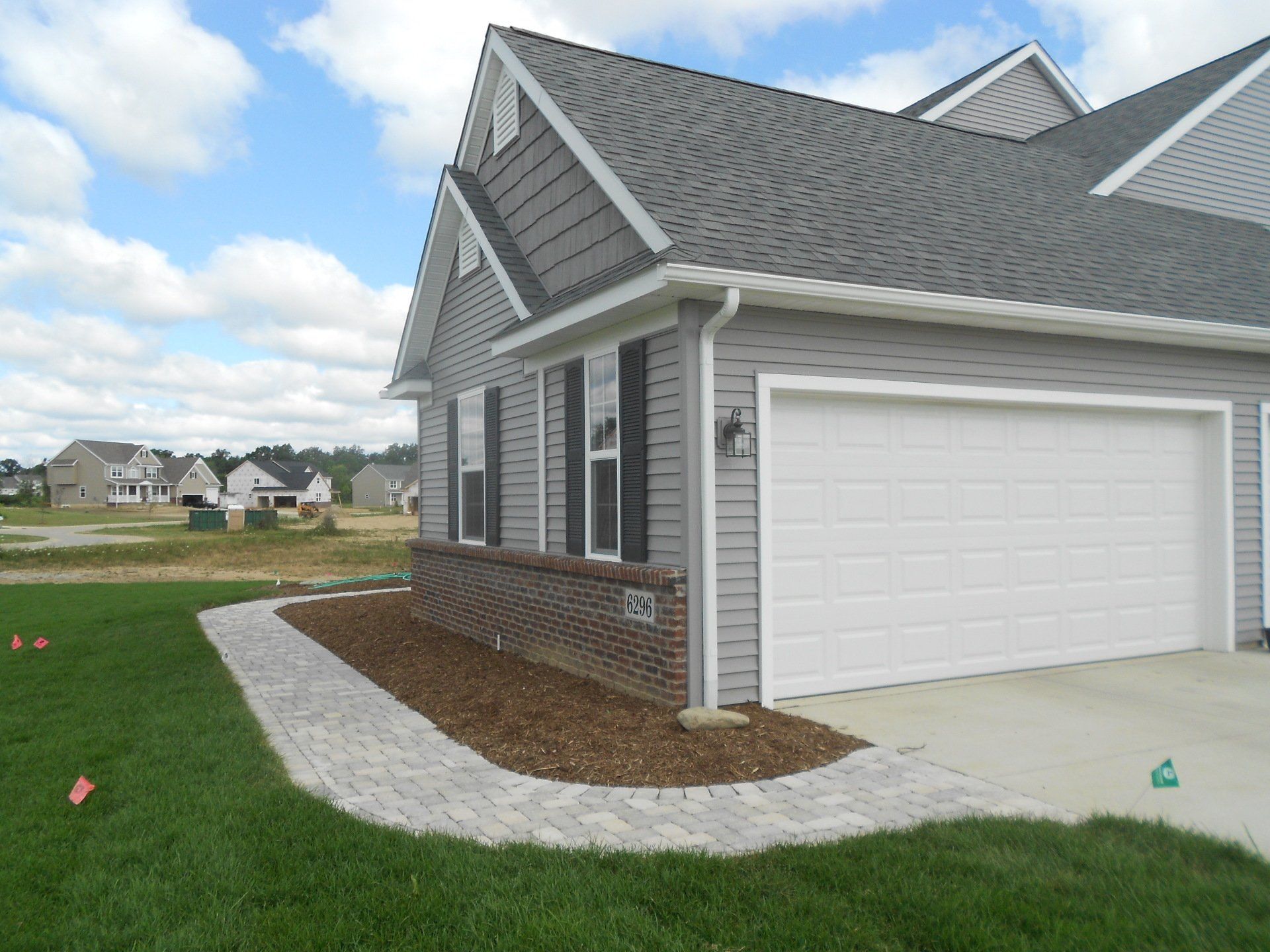 Suburban house exterior with gray siding, white garage, and curved concrete walkway beside a green lawn