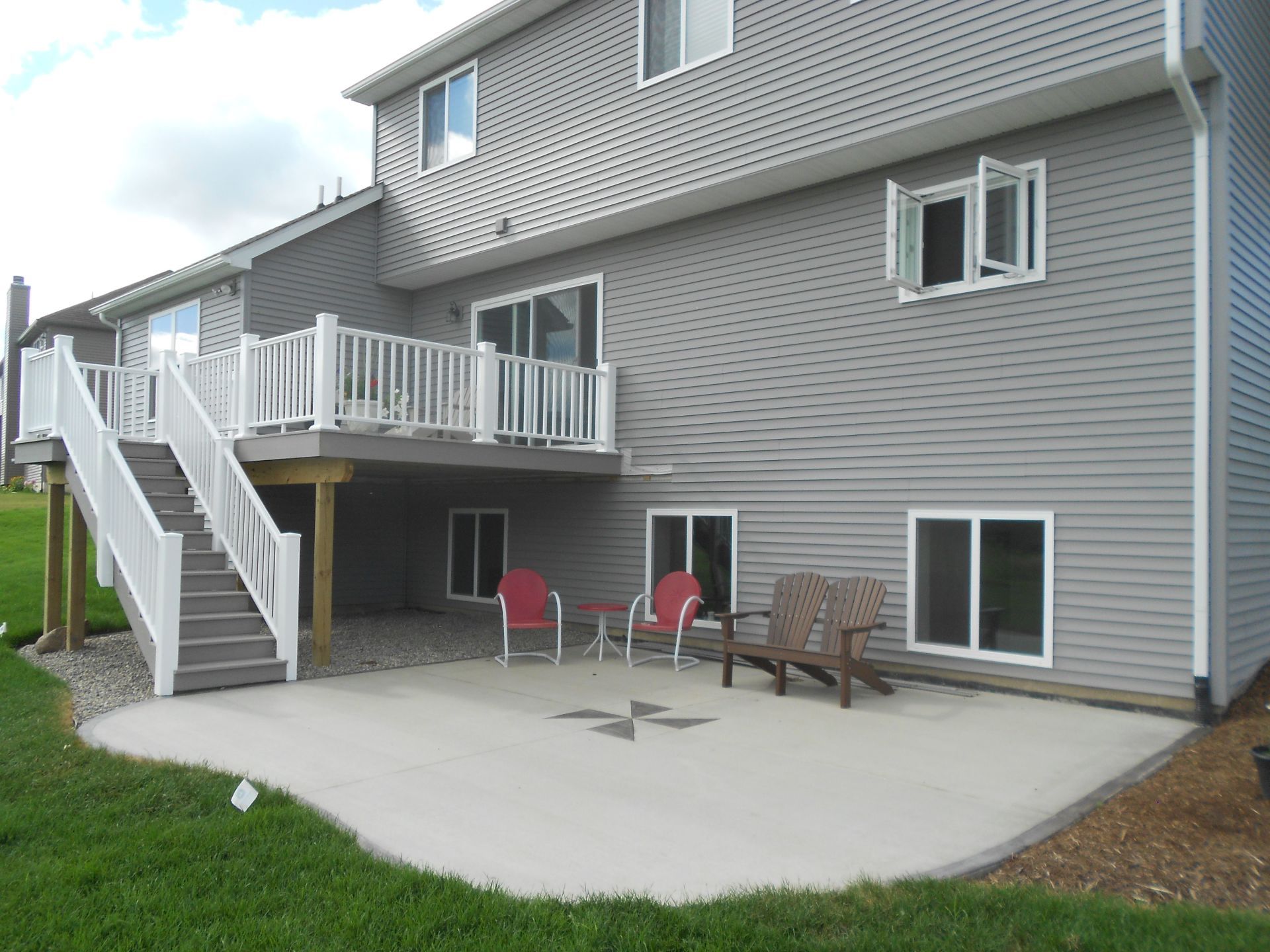 Apartment building exterior with white stairs, raised deck, and patio chairs on a concrete patio