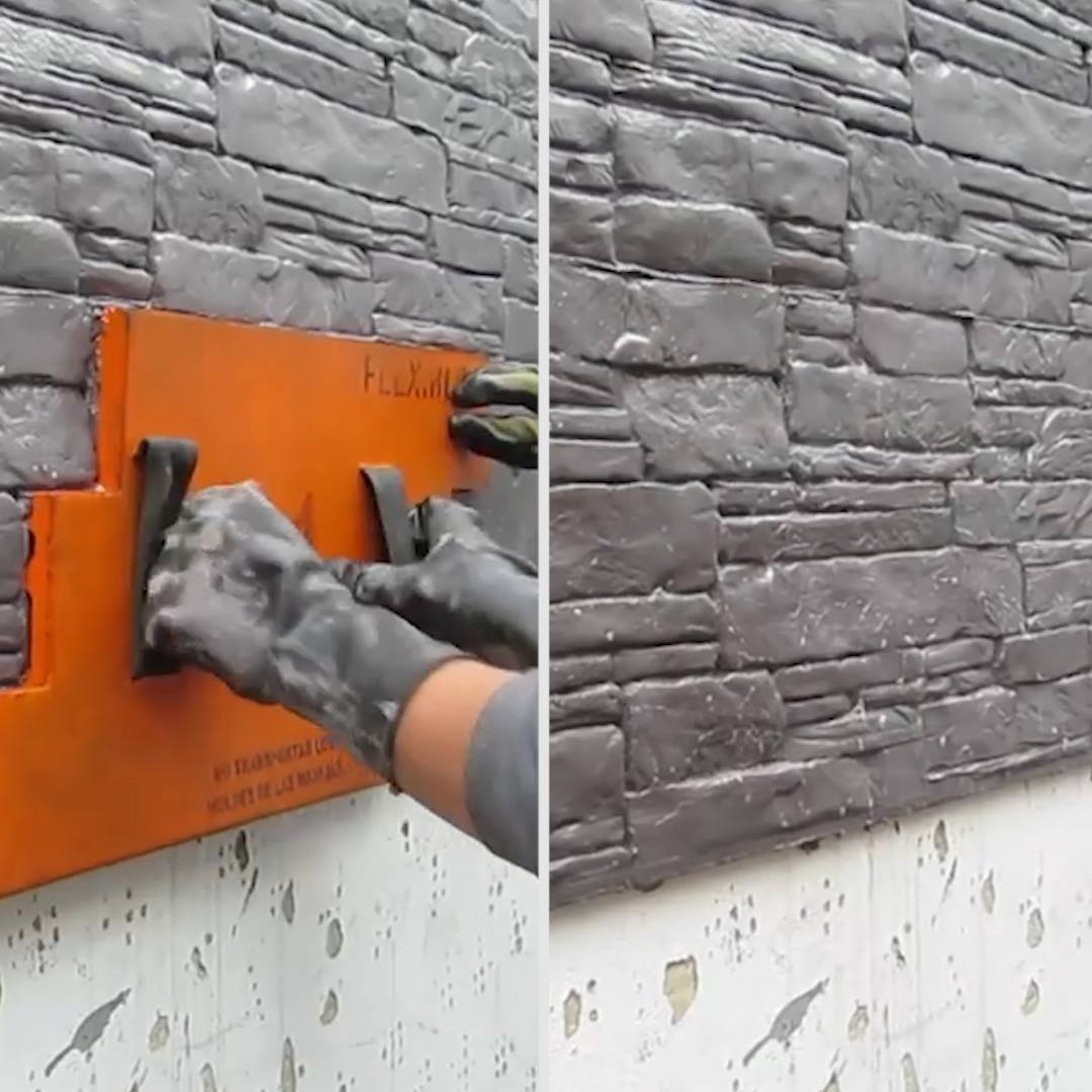 Gloved hands press an orange wall tile onto a gray stone wall facade.