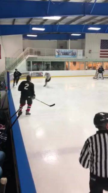 Indoor ice hockey game with players skating on the rink and a referee in the foreground