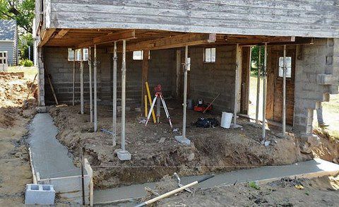 Foundation repair work under a raised house with support jacks and exposed dirt foundation