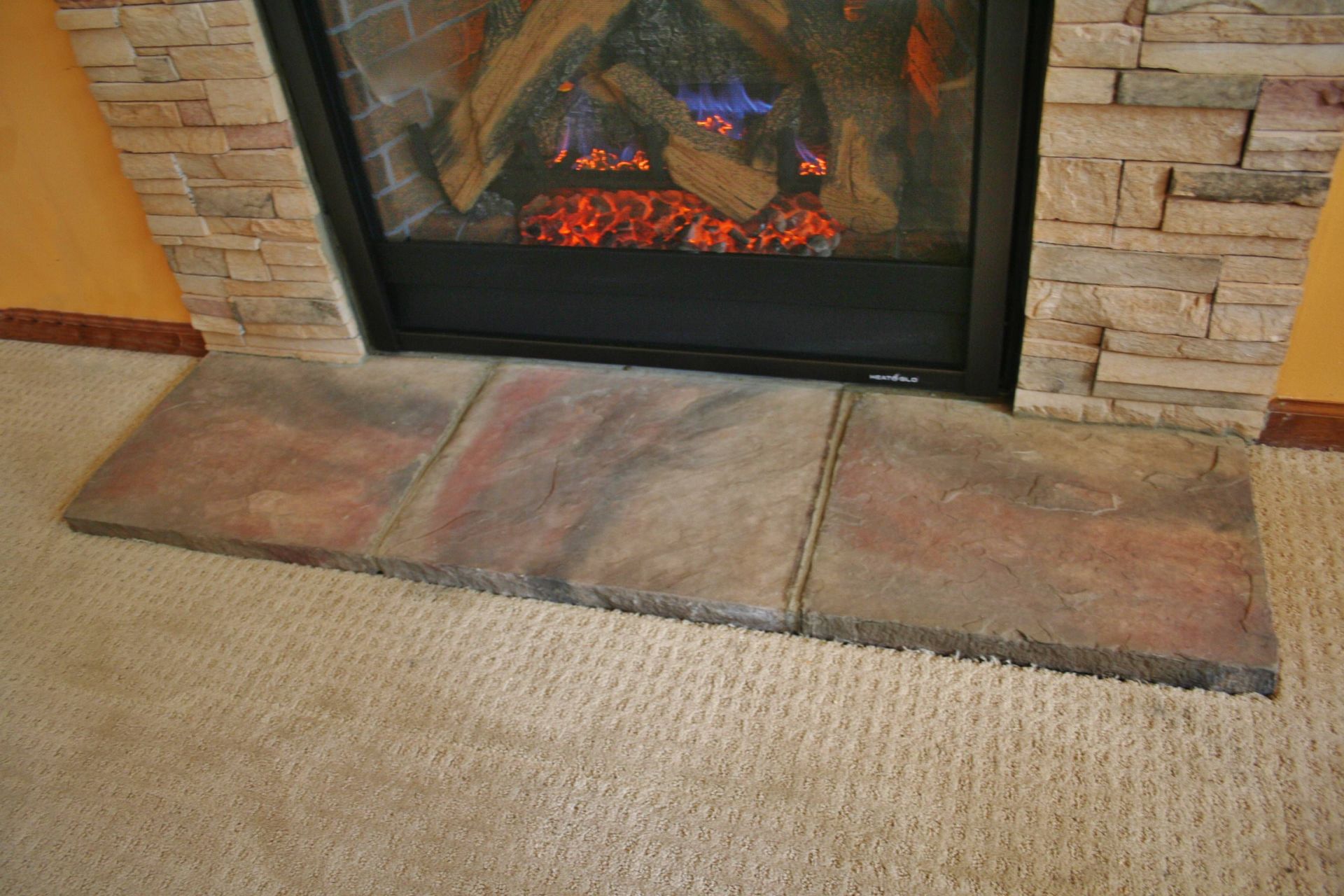 Stone fireplace with a glowing fire and a worn hearth beside beige carpet