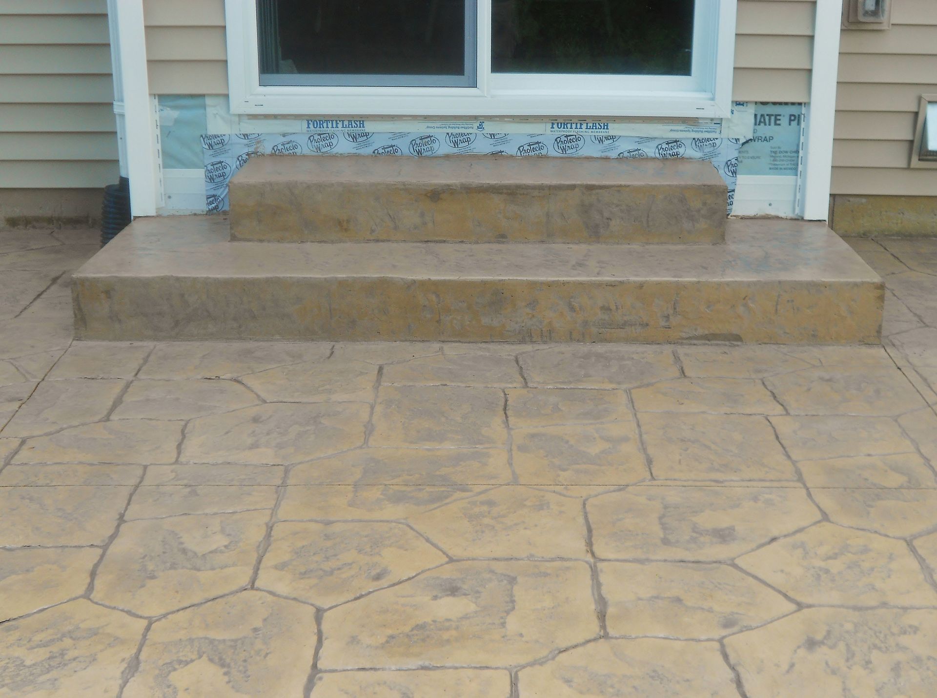 Front steps and stone patio leading to a house entrance with a glass door