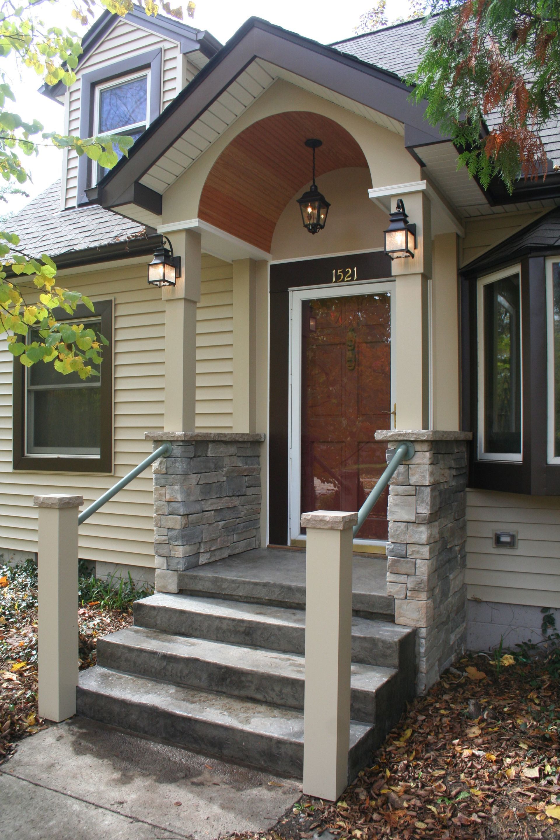 Front entrance with stone steps, wooden door, and arched porch on a beige house
