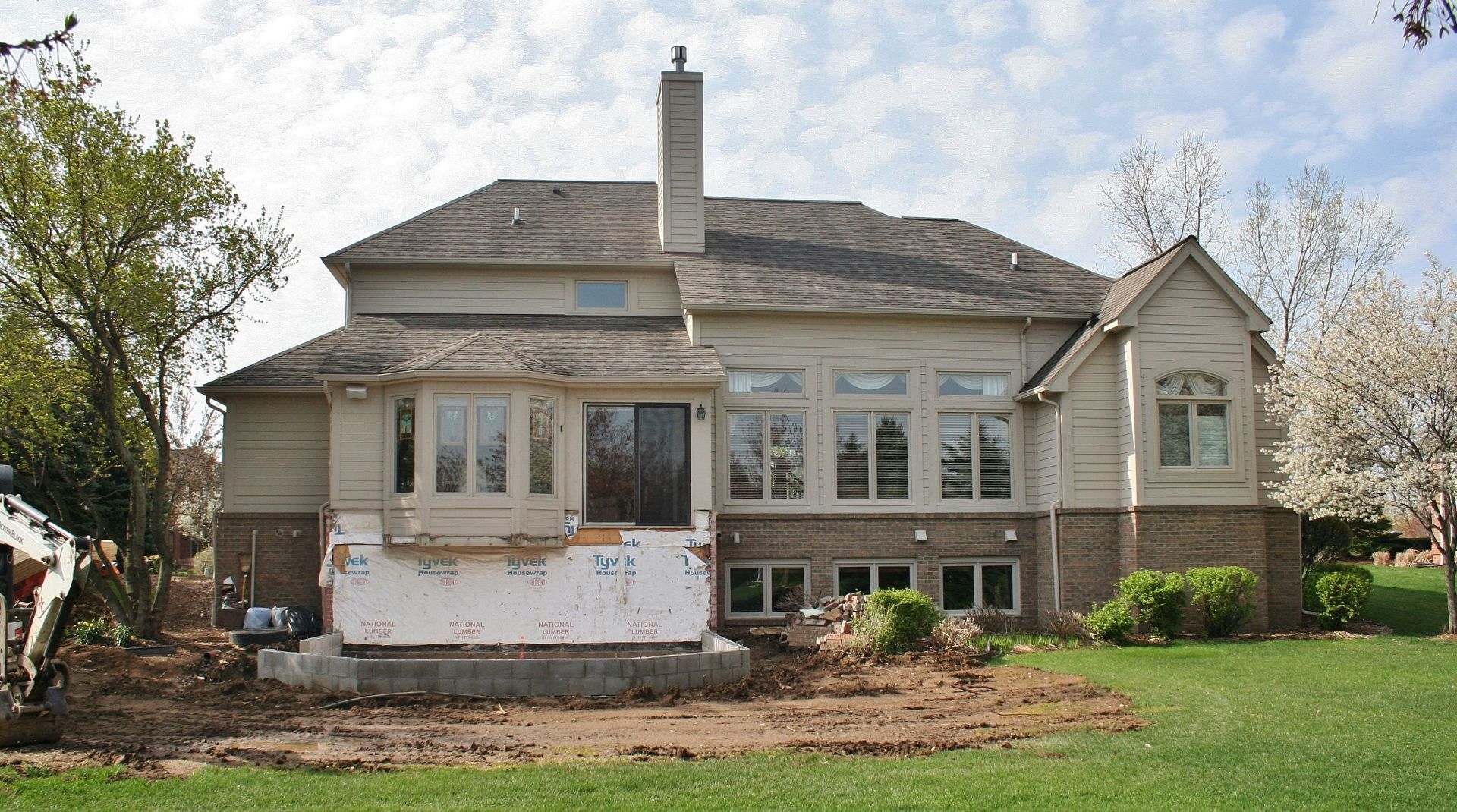 Suburban house exterior with damaged lower siding and a small front lawn