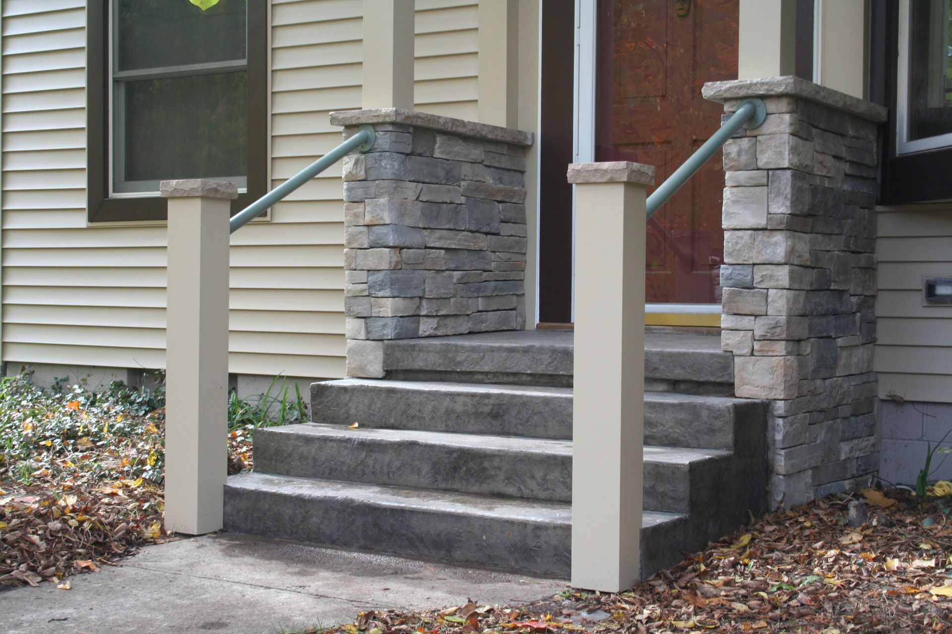 Front steps with stone veneer pillars and metal handrails leading to a house entrance