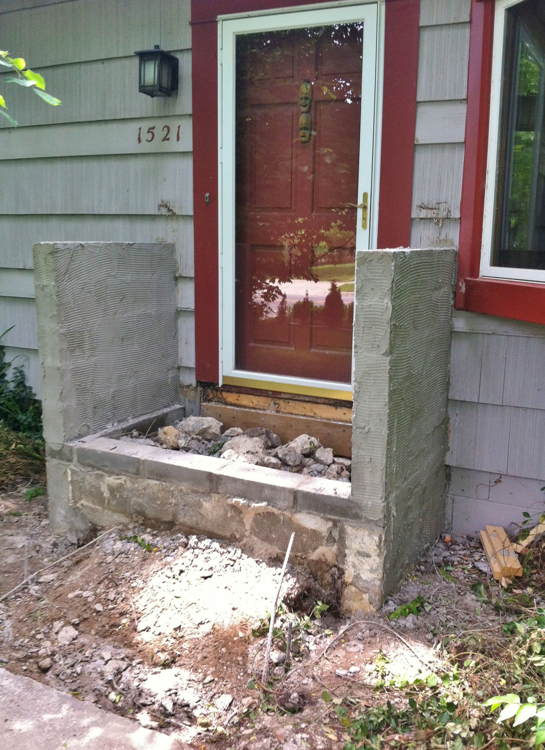 Front porch with a red door, damaged concrete steps, and rubble in front of a gray house.