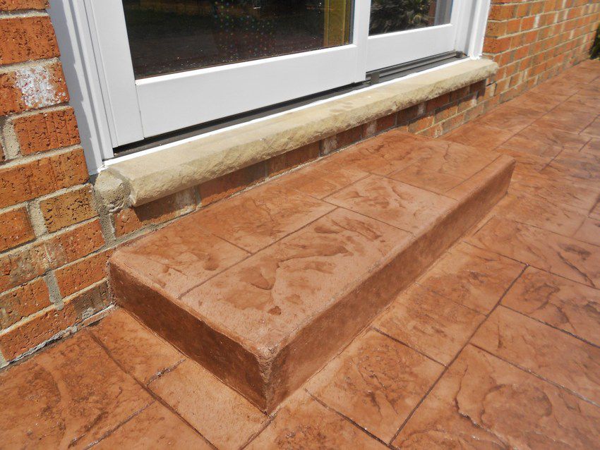 Brick step below a white door on a tiled patio, with a small ramp beside it