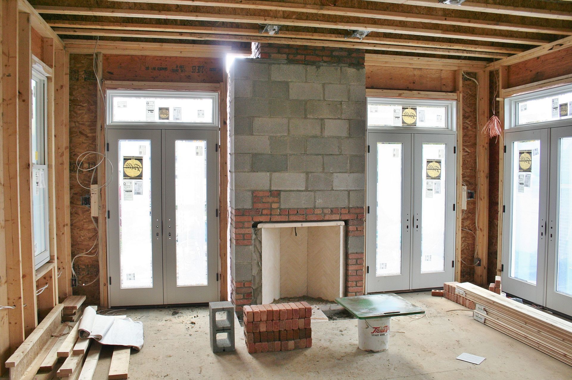 Unfinished room interior with exposed beams, cinder block fireplace, and French doors letting in daylight