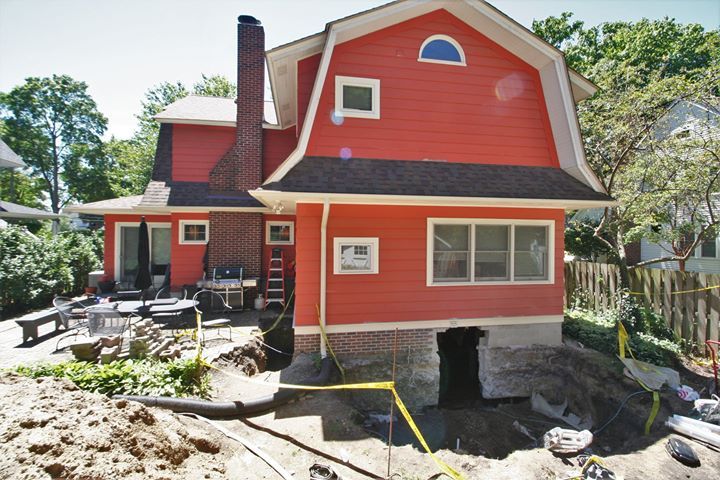 Red house with black roof and stone foundation beside a patio and rocky yard