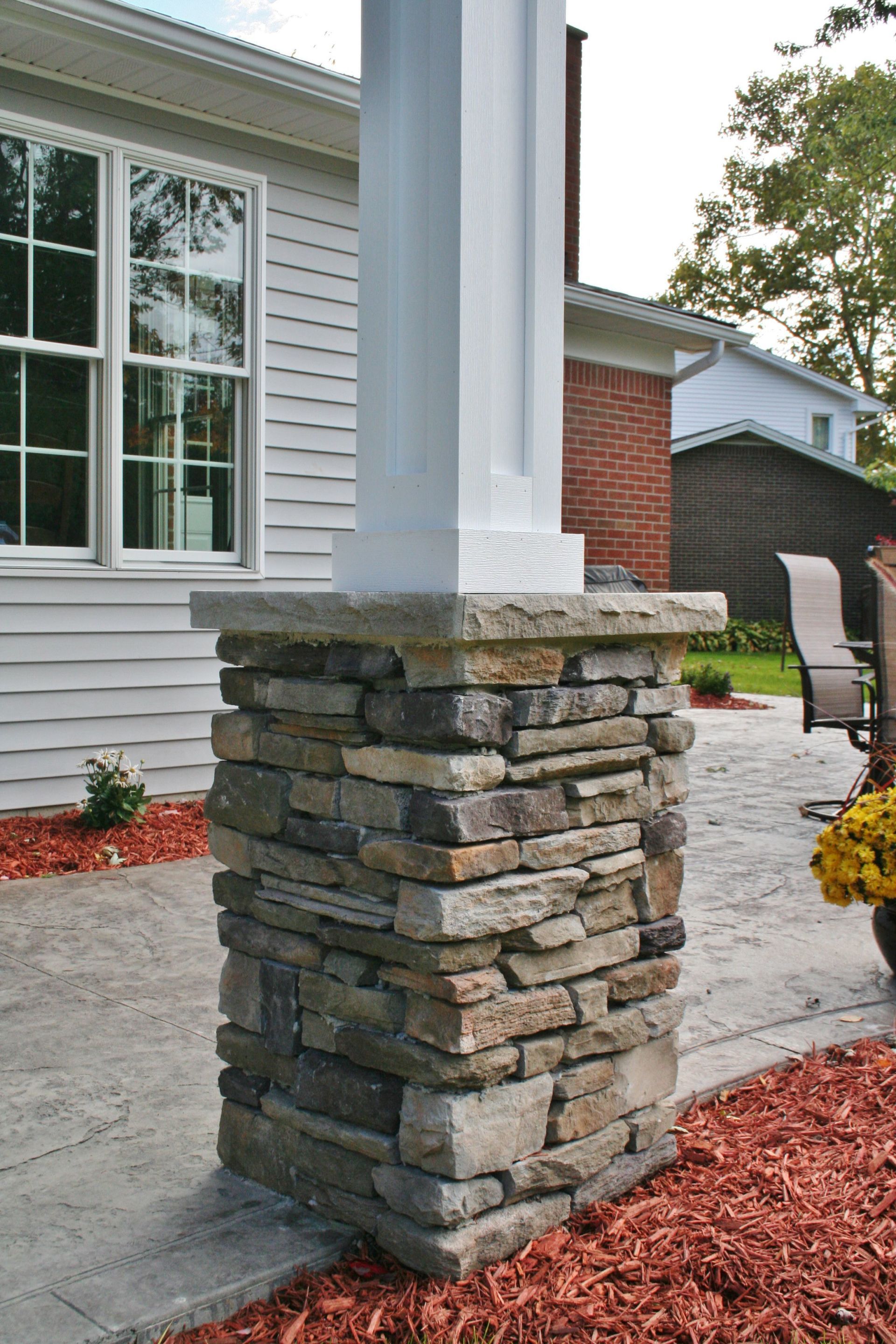 Stone-clad porch column beside a white house exterior with brick accent wall and concrete walkway