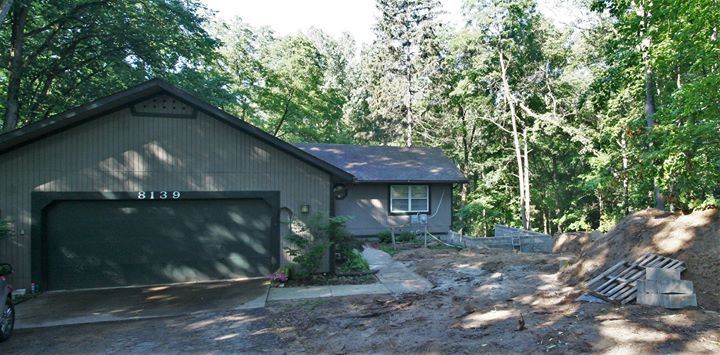Dark green garage house with driveway in a wooded area