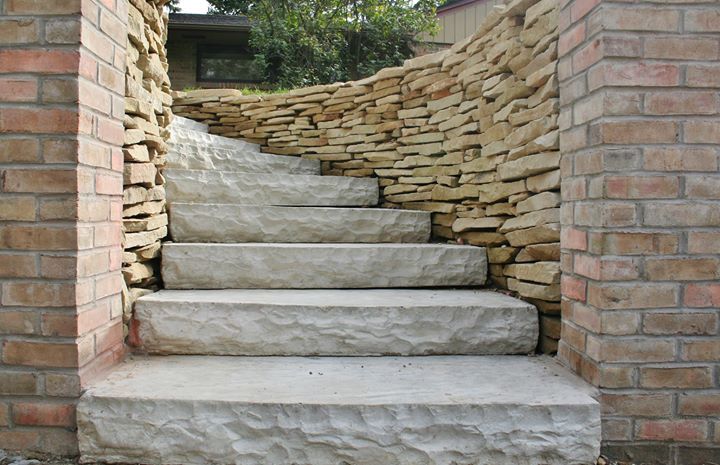 Stone steps between brick pillars leading up to a curved stone wall and garden path