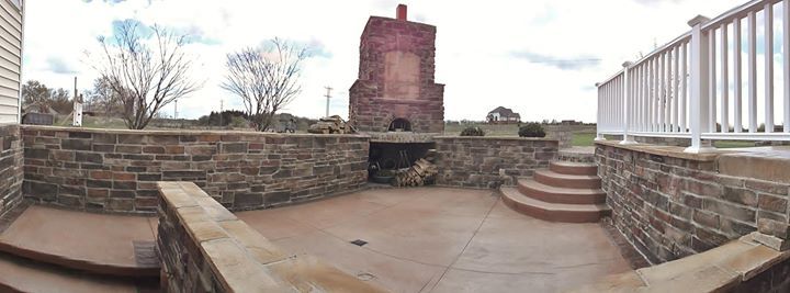 Stone rooftop terrace with low walls, steps, and a tall brick chimney under a cloudy sky