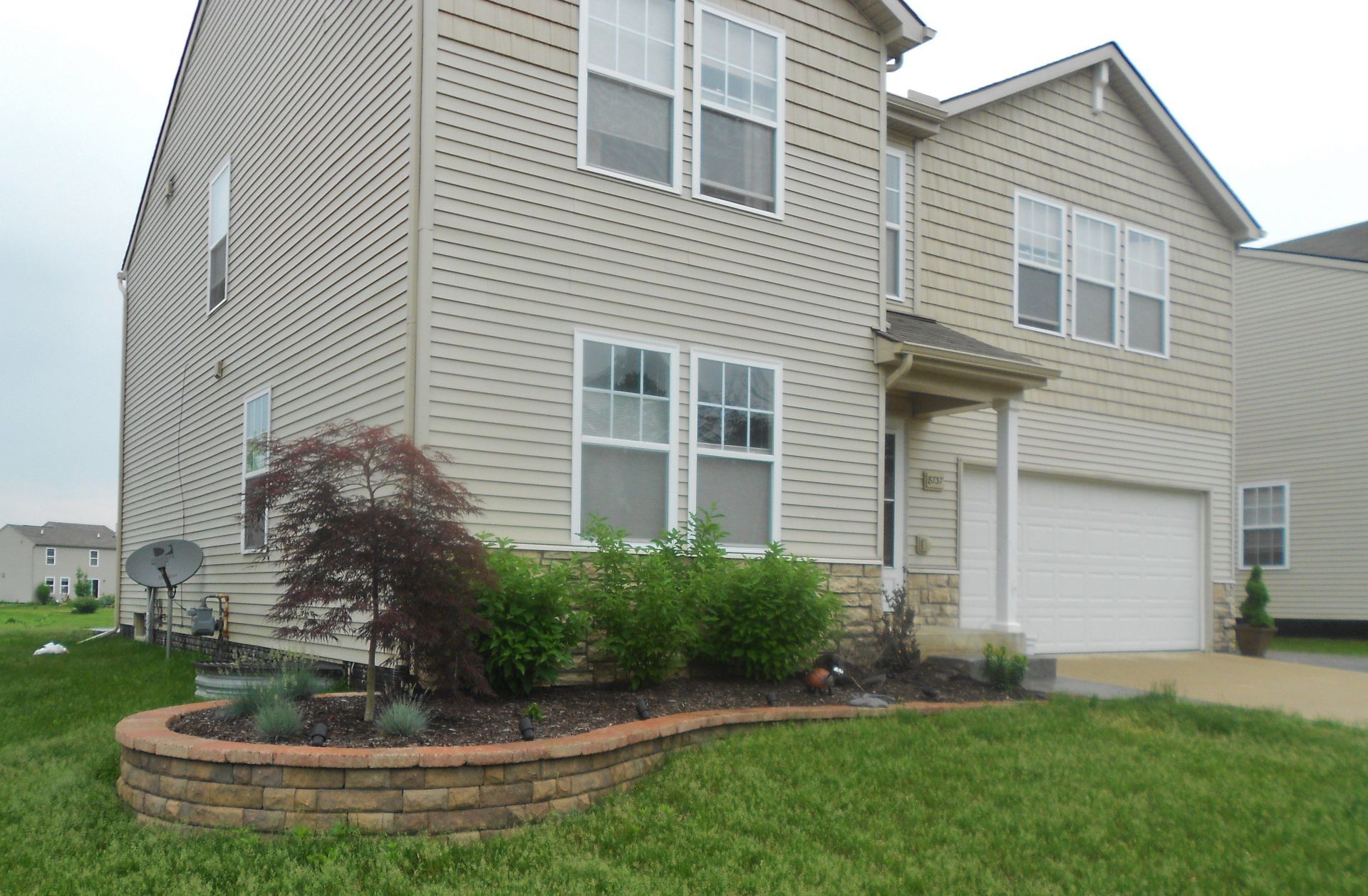 Suburban house exterior with beige siding, white garage, and landscaped front yard