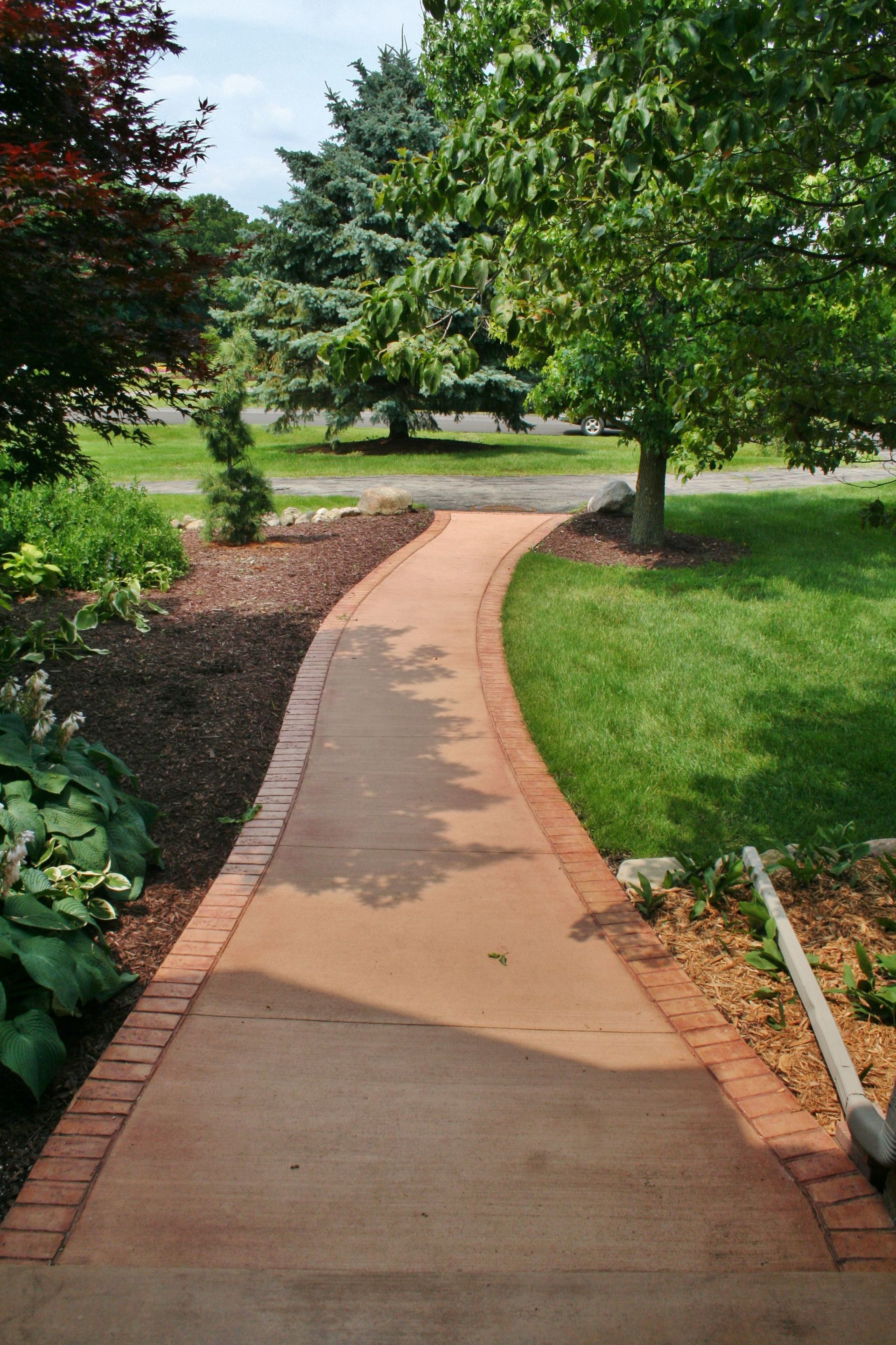 Curved concrete walkway through a green park with trees and flower beds