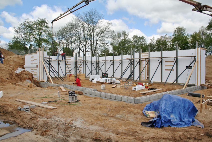 Construction site with workers, concrete foundation walls, and a crane over sandy ground