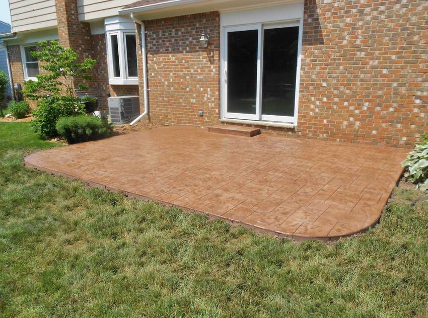 Backyard brick patio with large stamped concrete slab beside a house and sliding glass doors