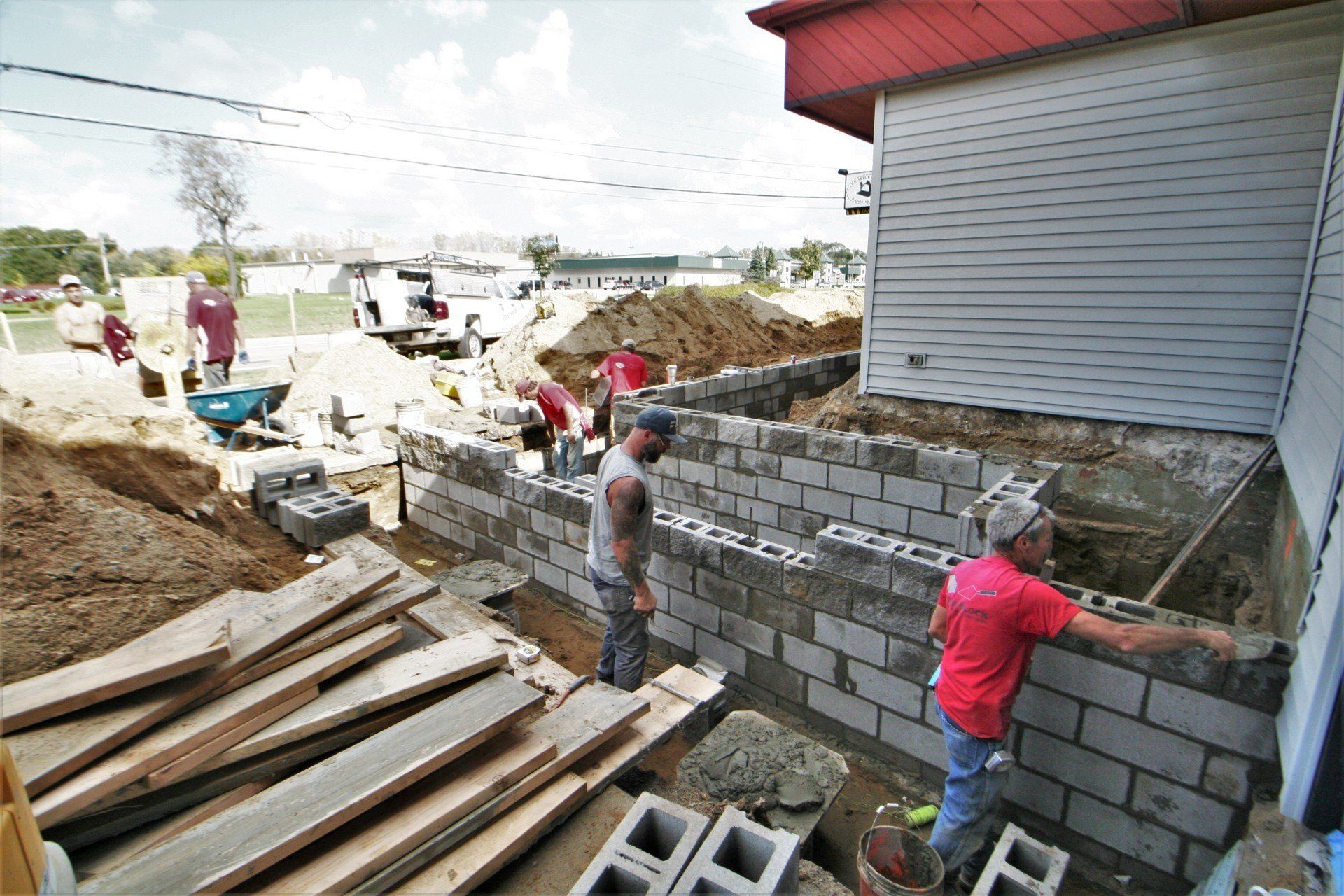 Workers building a gray cinder block wall beside a house at a construction site