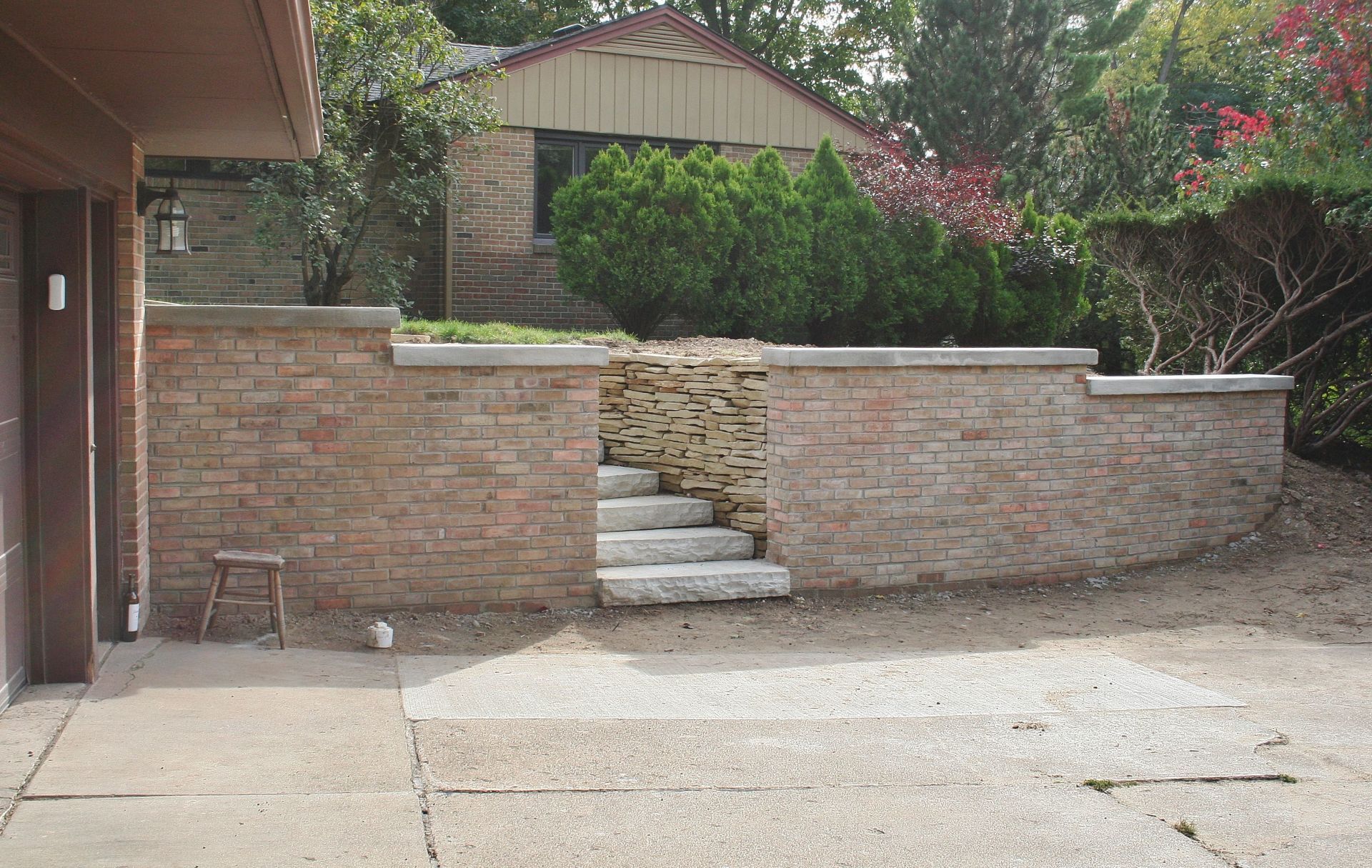 Brick retaining wall with central stone steps leading to a raised yard and shrubs behind it