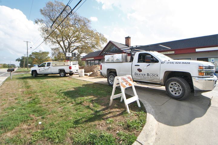 Utility trucks parked outside a house with a white barricade on the driveway.