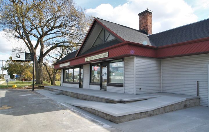 Empty storefront with gray siding, red trim, and a raised sidewalk under leafless trees.