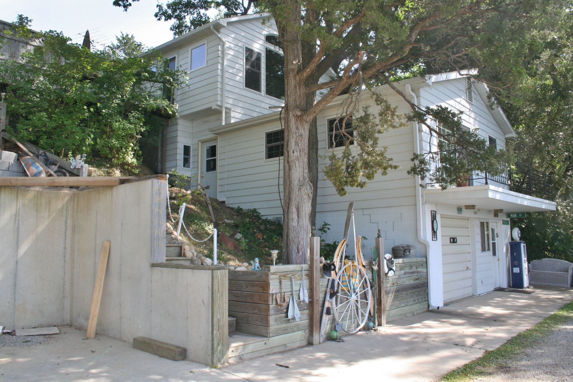 Residential hillside house with a tree, retaining wall, and garage under a bright sky