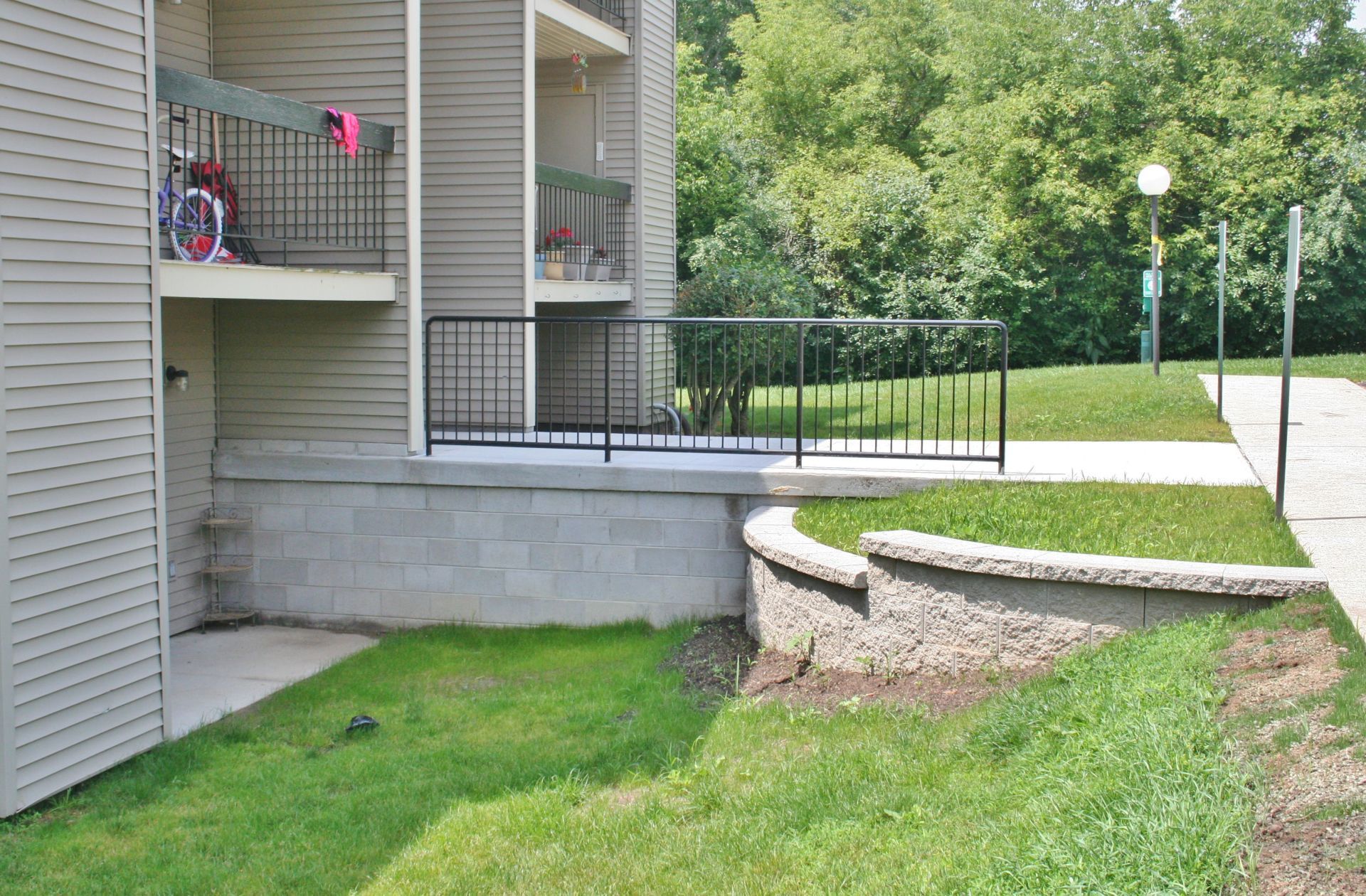 Apartment building patio with grass, stone retaining wall, and a balcony with a pink bicycle.