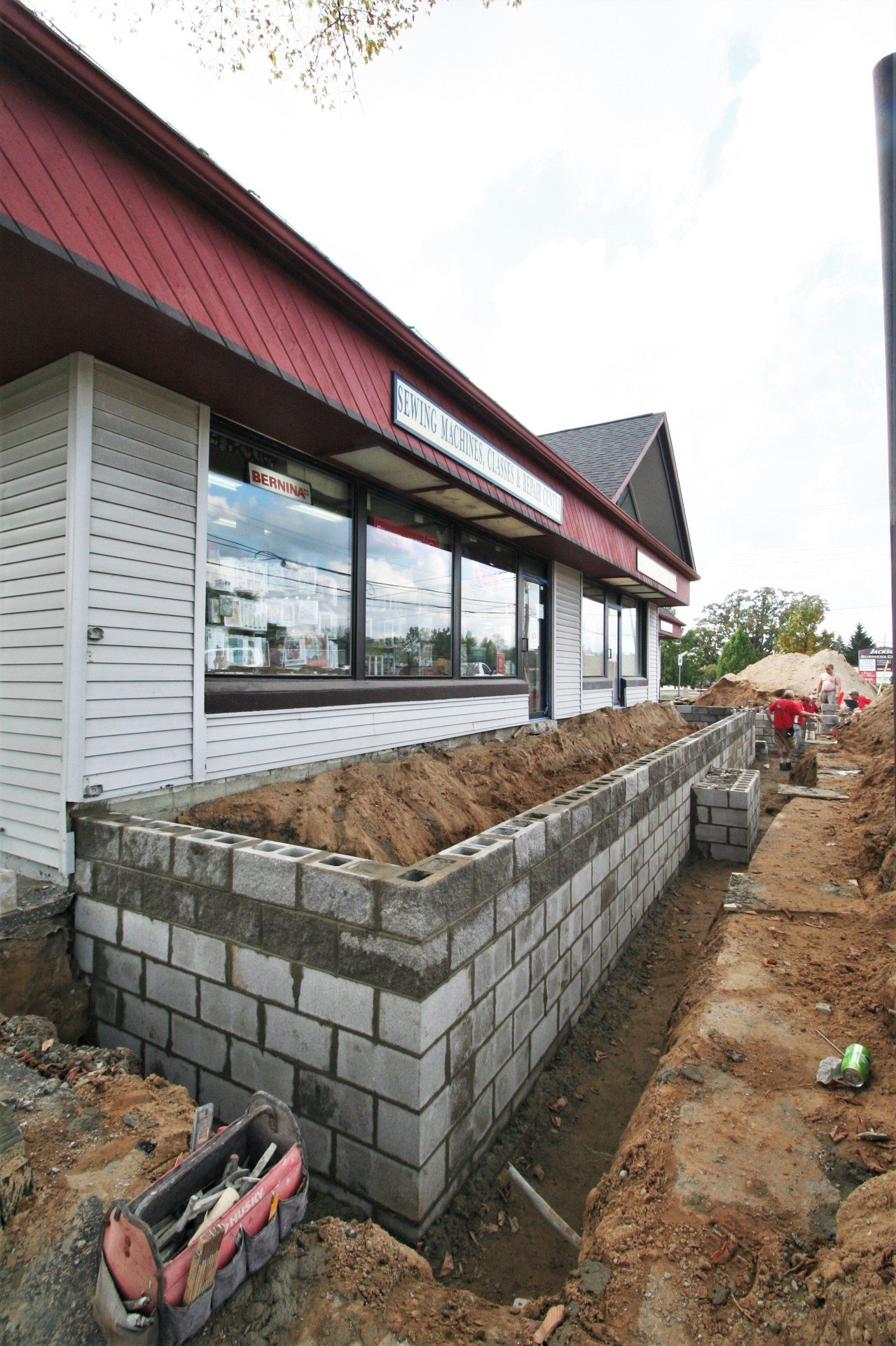 Exterior of a building with a raised cinderblock planter and construction work along the side path
