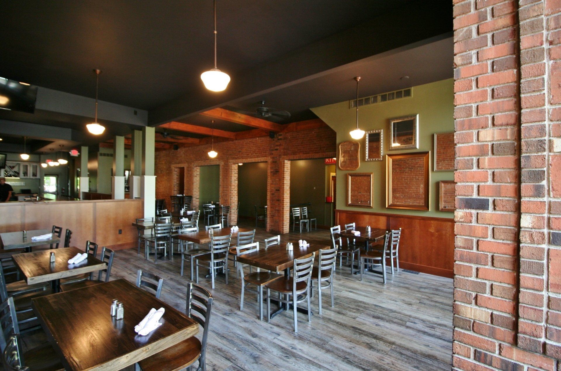Empty restaurant dining area with metal chairs, wooden tables, brick walls, and hanging lights