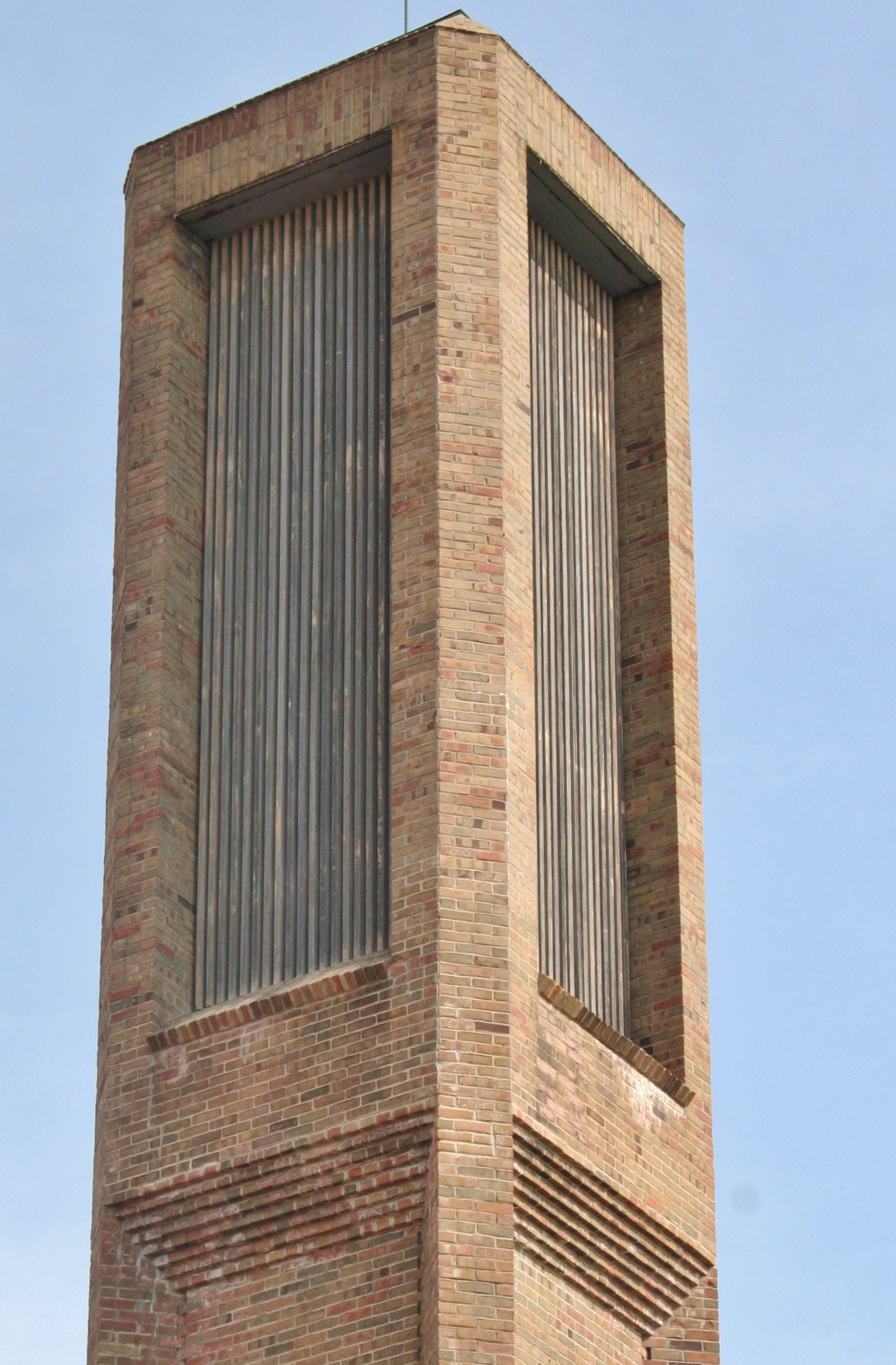 Tall brick tower with vertical metal louvers against a blue sky