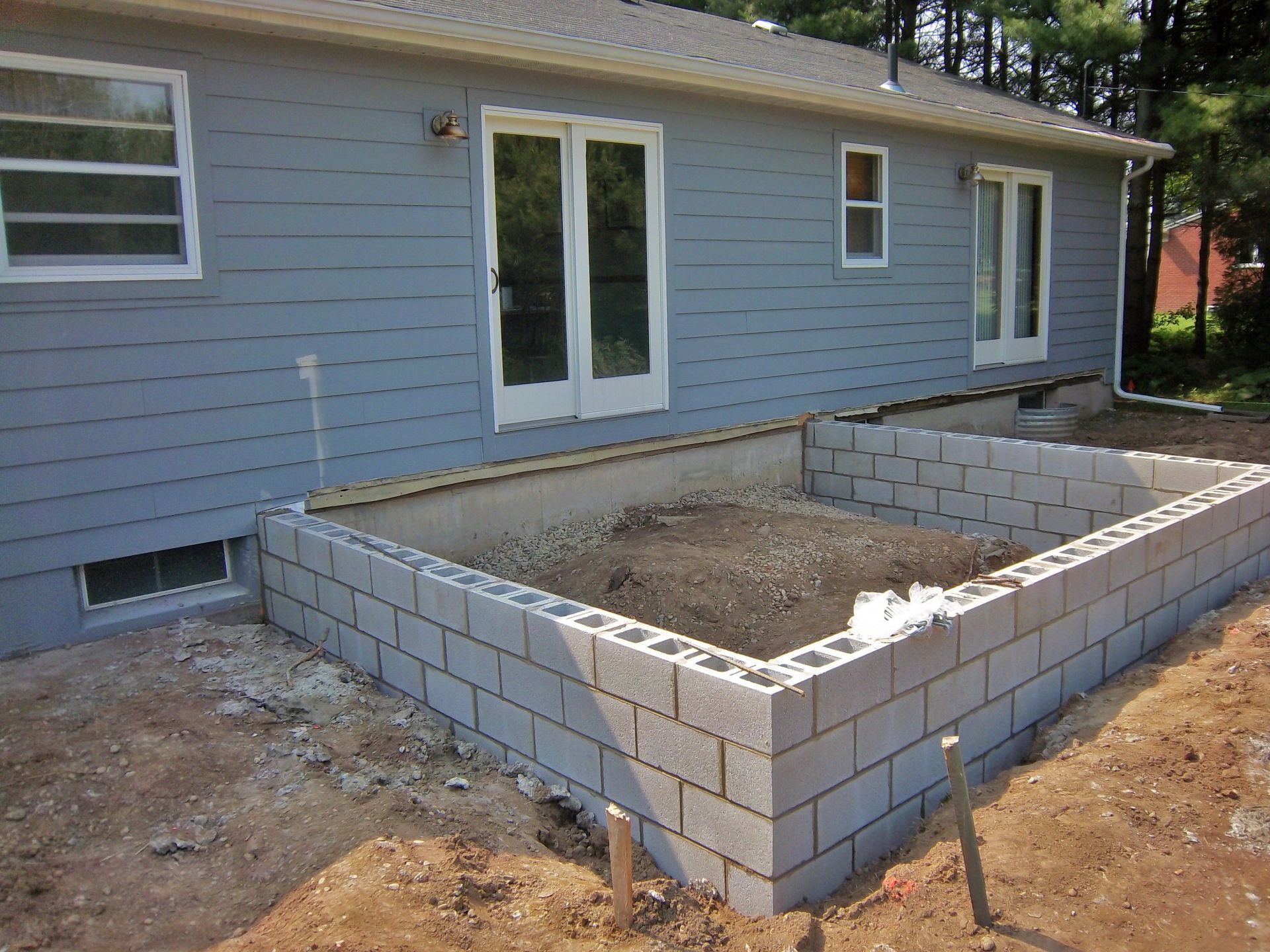 Backyard construction site with a new cinder block foundation beside a gray house