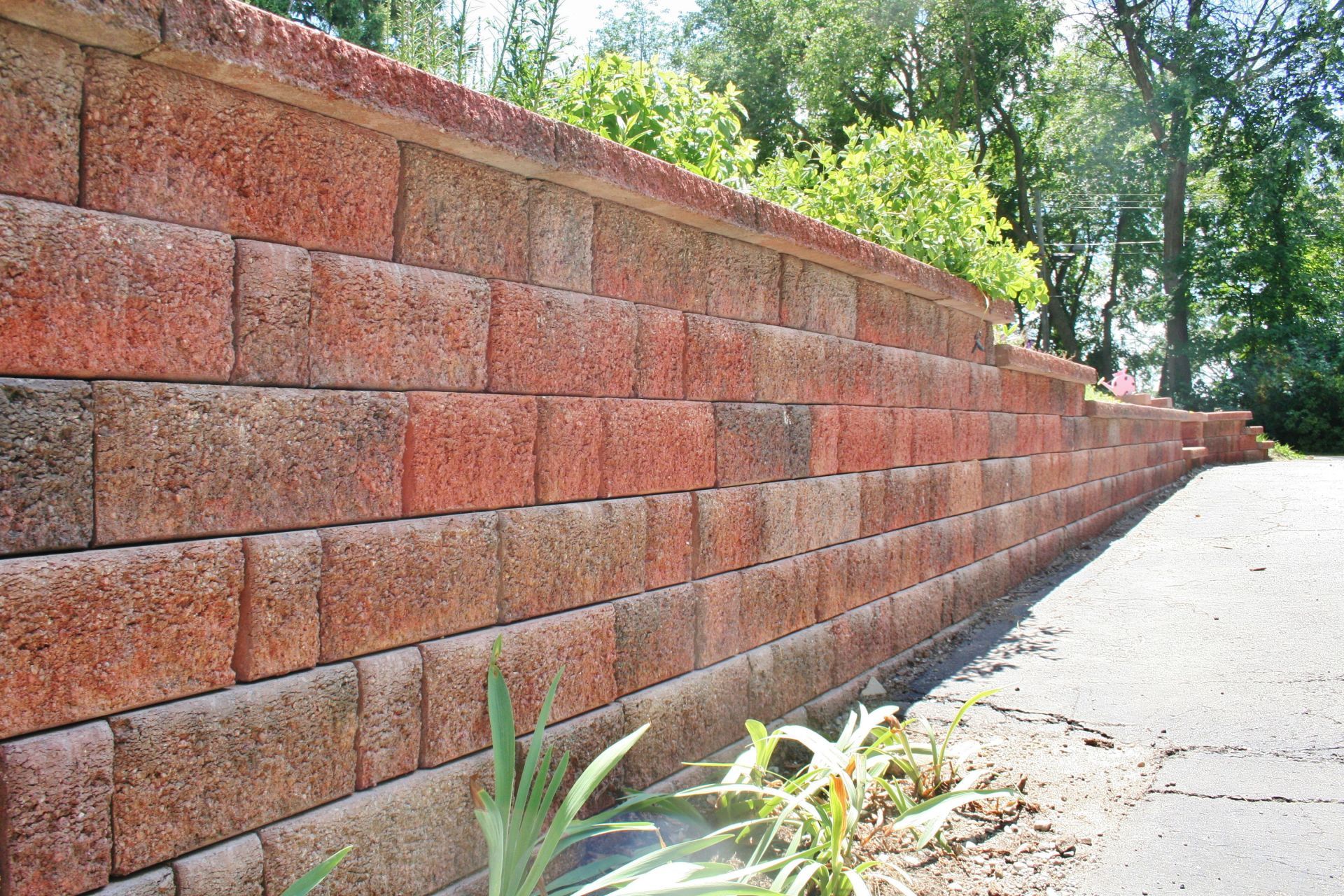Brick retaining wall along a paved path beside trees and greenery