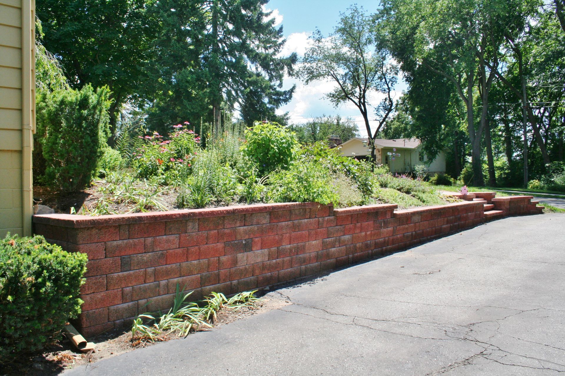 Brick retaining wall along a landscaped garden beside a paved road under trees