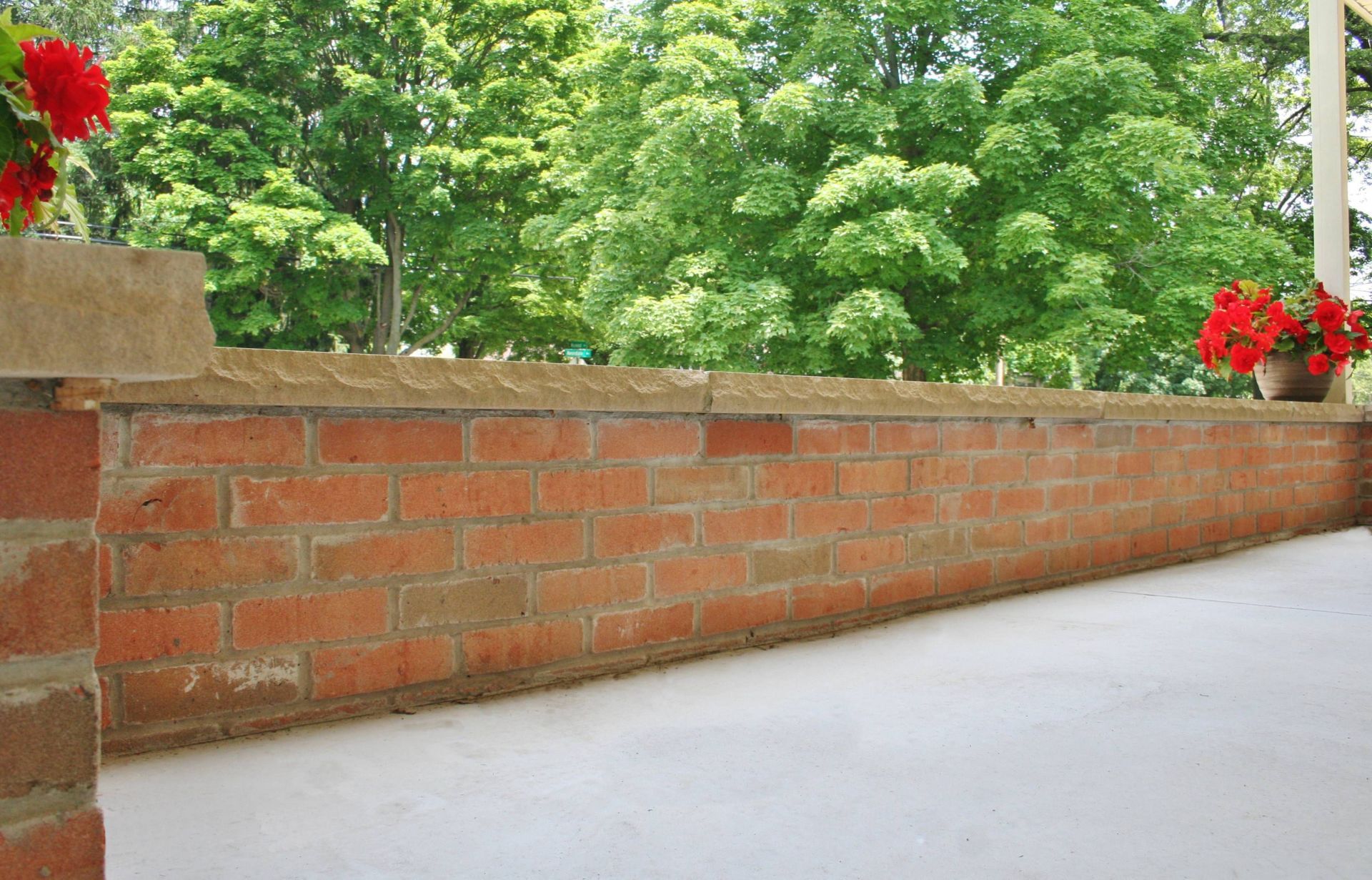 Brick balcony wall with red flowers and green trees in the background