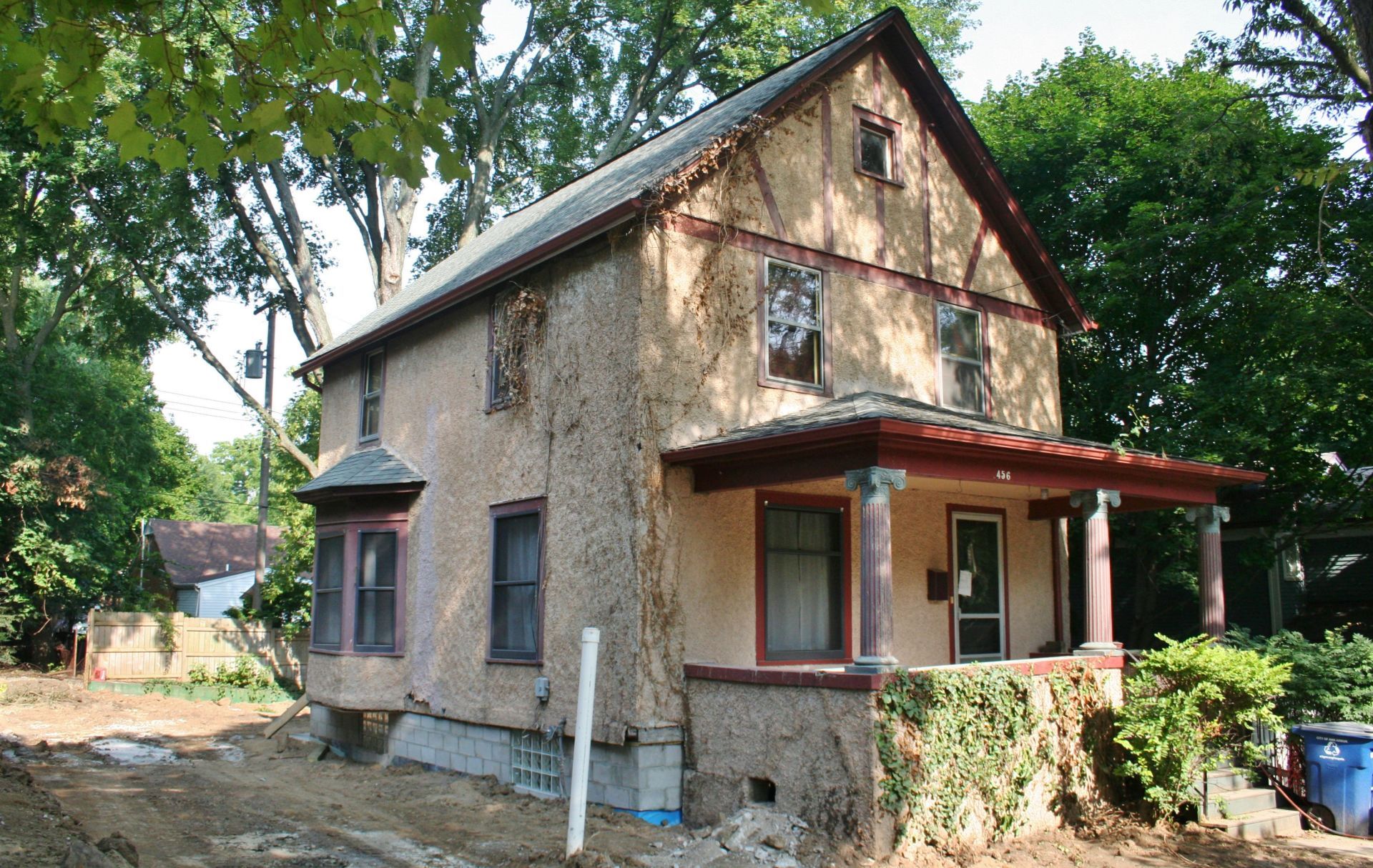 Old weathered house with peeling stucco, small porch, and trees surrounding it