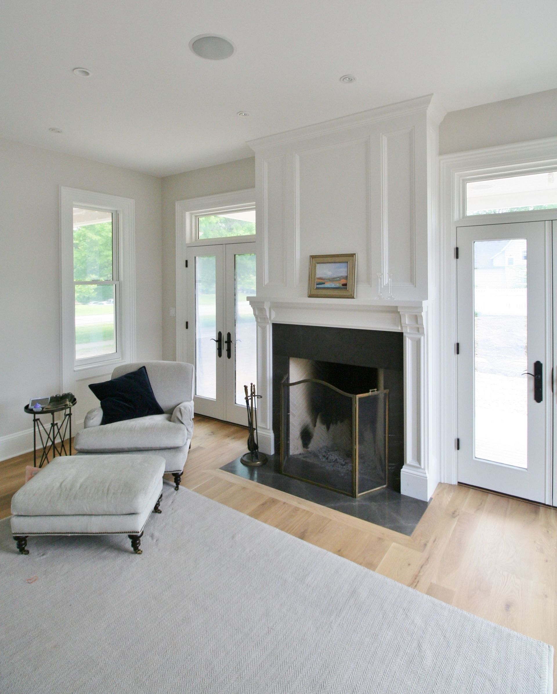 Bright living room with white fireplace, armchair, ottoman, and French doors