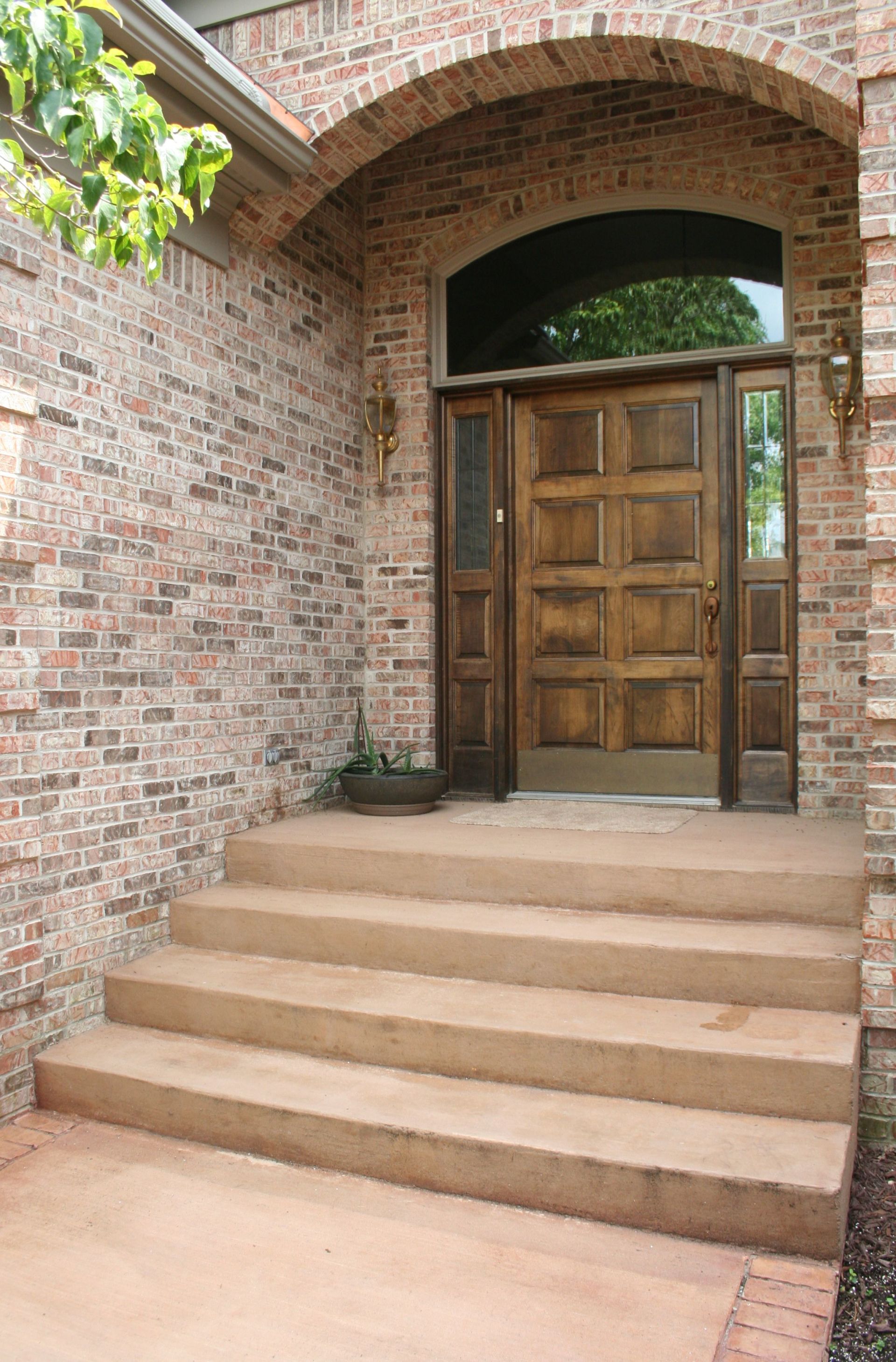 Brick entryway with steps leading to a wooden double door under an arched brick archway