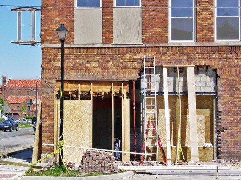 Brick building under renovation with exposed framing, ladder, and tools at the front entrance