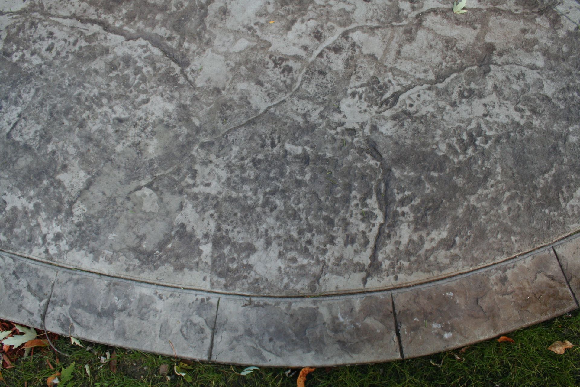 Weathered gray stone surface with cracks and a curved edge beside grass