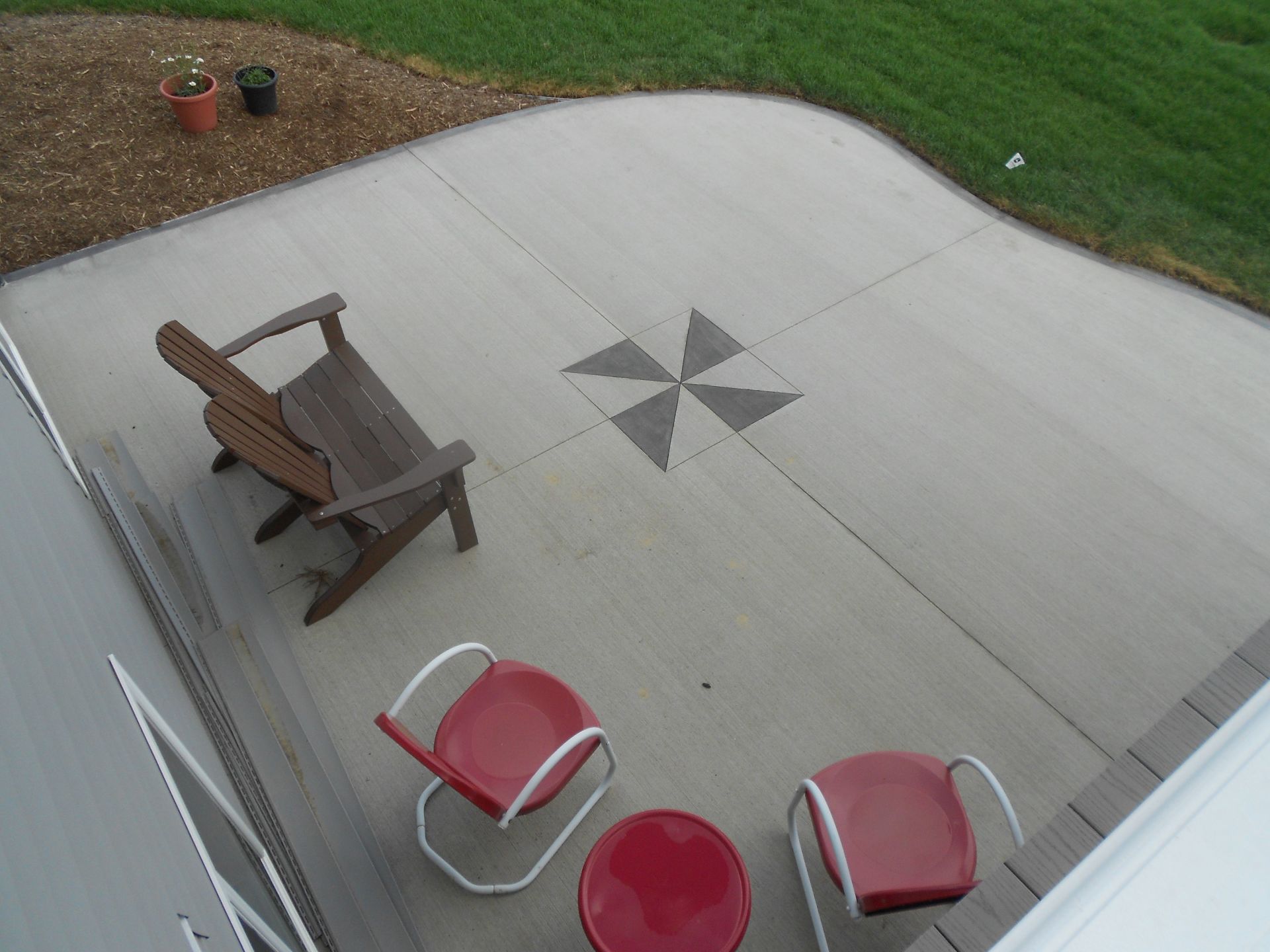 Patio with a wooden chair and two red seats around a star-patterned concrete slab
