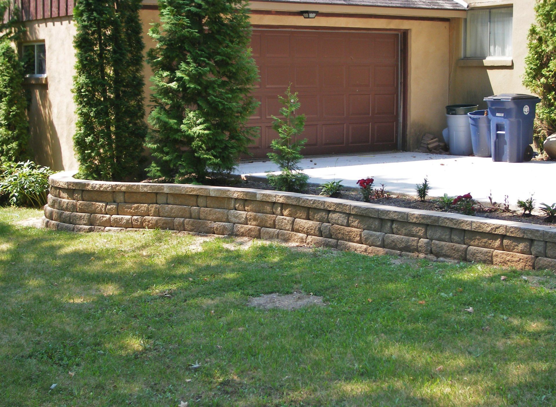 Front yard with stone retaining wall, green lawn, and a driveway in front of a garage