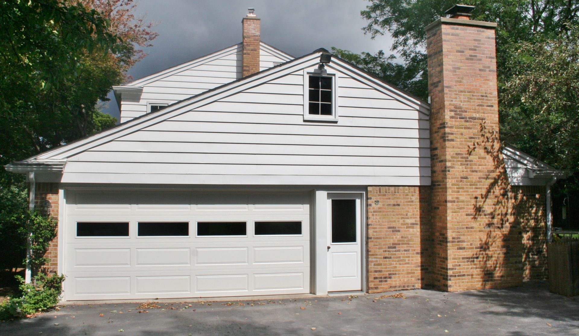 Suburban house with white siding, garage, brick chimney, and front door under a cloudy sky