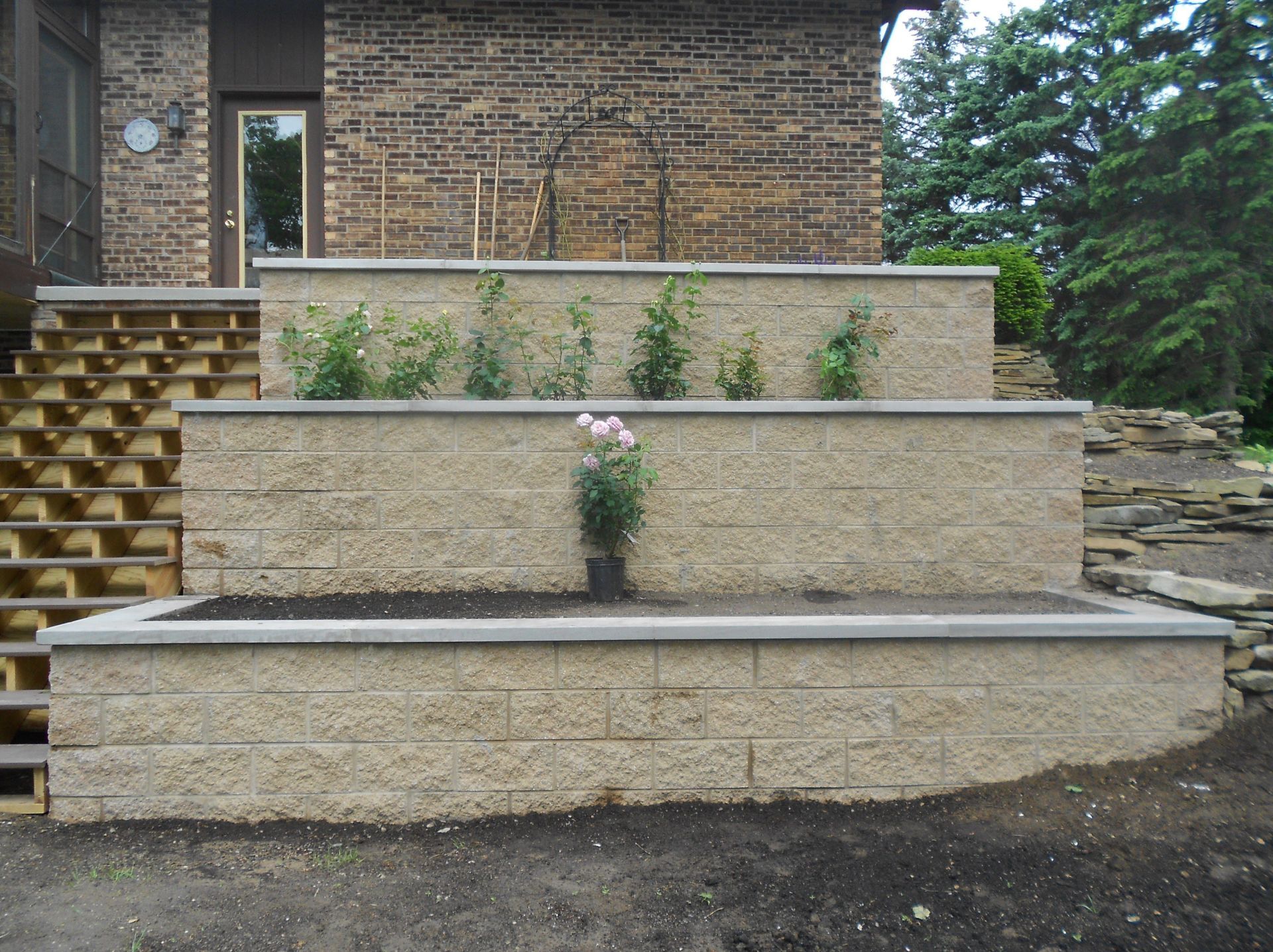 Tiered stone planter wall with sparse flowers in front of a house entrance