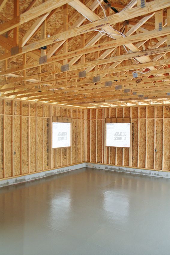 Empty unfinished room with exposed wooden framing, two windows, and a concrete floor